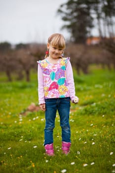 Cute little girl standing on a green field with flowers