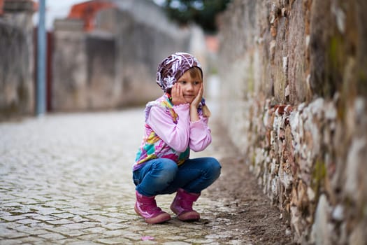 Portrait of a little girl outdoors on a city street, hands on cheeks