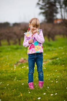 Cute little girl standing on a green field with flowers