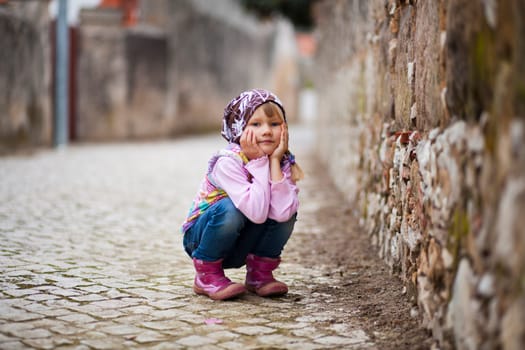 Portrait of a little girl outdoors on a city street, hands on cheeks