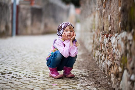 Portrait of a little girl outdoors on a city street, hands on cheeks