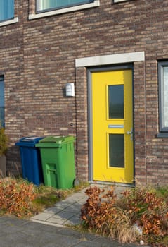 yellow front door and a blue and green trash can for separate trash
