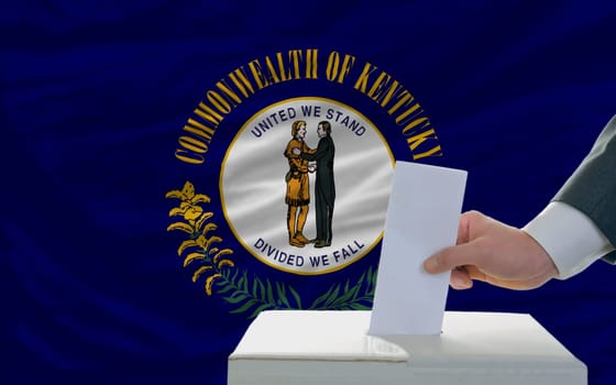 man putting ballot in a box during elections  in front of flag american state of kentucky