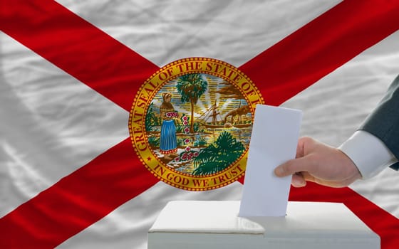 man putting ballot in a box during elections  in front of flag american state of florida