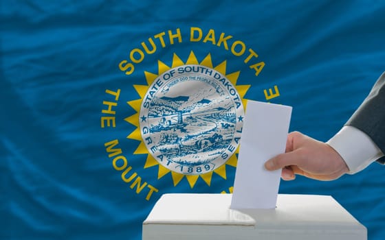 man putting ballot in a box during elections  in front of flag american state of south dakota