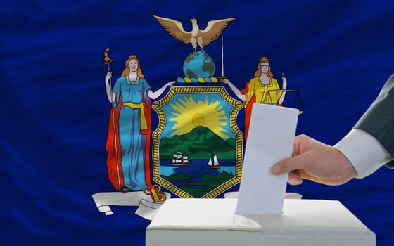 man putting ballot in a box during elections  in front of flag american state of new york
