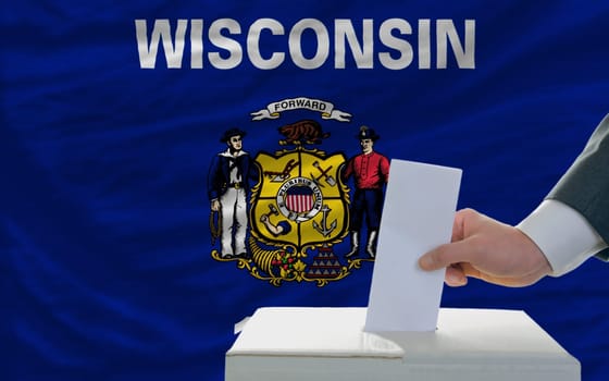 man putting ballot in a box during elections  in front of flag american state of wisconsin