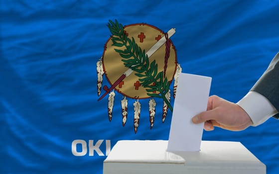 man putting ballot in a box during elections  in front of flag american state of oklahoma