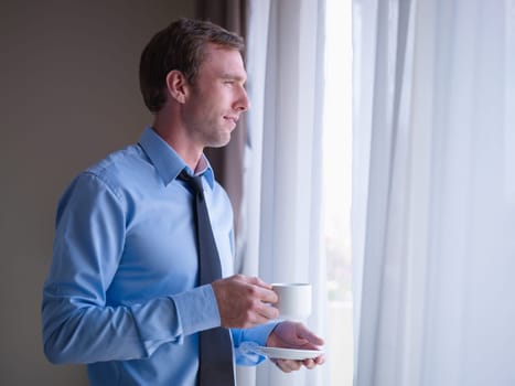 Mid adult business man relaxing and drinking a cup of tea, looking out of window. Side view, copy space