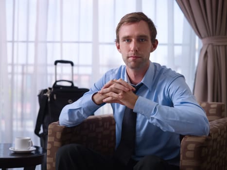 Portrait of happy caucasian businessman with crossed fingers smiling at camera in hotel room during business trip. Front view