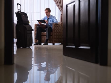 Mid adult caucasian manager typing on tablet pc in hotel room during business travel. Low angle view, full length