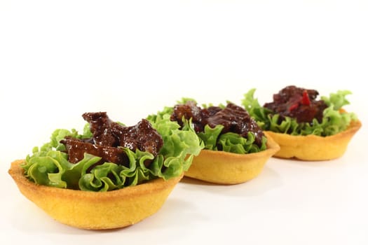 Corn tartlets with beef salad against a white background
