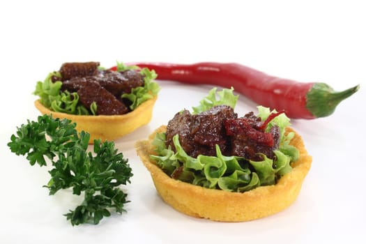 Corn tartlets with beef salad against a white background