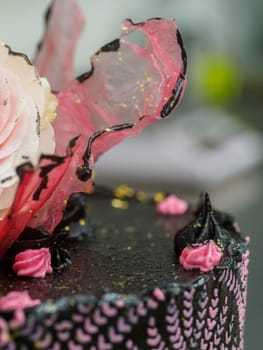 frosted icing black decorate cake for birthday celebration, real rose topping and pink sweet swirls in professional kitchen