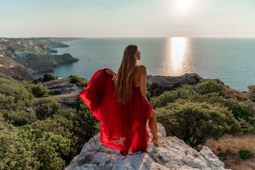 Woman sunset sea red dress, back view a happy beautiful sensual woman in a red long dress posing on a rock high above the sea on sunset