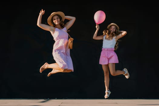 mother and daughter jumping in pink dresses with loose long hair on a black background. Enjoy communicating with each other.