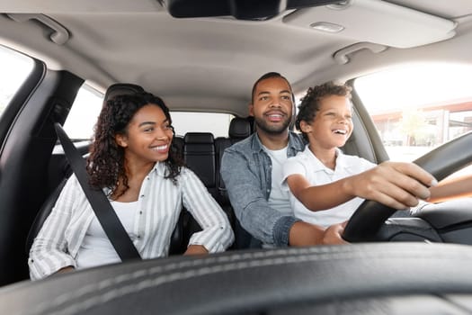 African American Father Teaching His Son To Drive Driving The Car Together. Happy Family Riding New Automobile In City, Having Fun Traveling By Auto. Vehicle Transportation