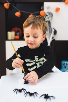 A child dressed as a skeleton shows spider and ghost crafts. Halloween party.