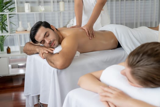 Caucasian couple customer enjoying relaxing anti-stress spa massage and pampering with beauty skin recreation leisure in day light ambient salon spa at luxury resort or hotel. Quiescent