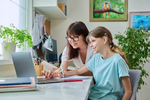 Mother helping preteen daughter to study, looking at laptop computer at desk together at home. Family, home lifestyle, school, education, study, kids concept