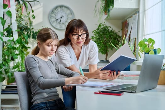 Mother helping preteen daughter to study, looking at laptop computer at desk together at home. Family, home lifestyle, school, education, study, kids concept