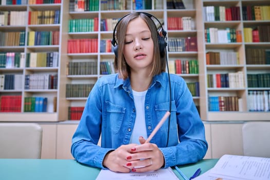 Close-up webcam view of face female student in headphones, inside university library. Young woman looking at camera online chat conference broadcast video recording. Internet technology for learning