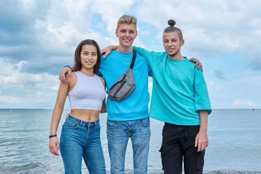 Portrait of cheerful teenage friends hugging outdoor, happy young people posing looking at camera on beach. Youth, team, summer vacation, communication, leisure, friendship, fun, lifestyle, holiday