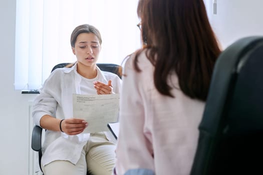 Female teenager at therapy meeting with professional psychologist terapist. Young sad serious girl showing formal mail letter. Psychology, psychotherapy, counseling, mental health of adolescents