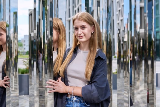 Portrait of young beautiful teenage female in modern city, fashionable smiling girl with long hair looking at camera, on mirror architecture. Beauty, fashion, youth, urban style concept