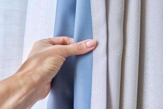 Close-up of woman's hand showing light gray curtain on blue opaque lining, fabric blackout