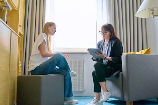 Young female at therapy meeting with psychotherapist. Session of teenage student girl, specialist psychologist with digital tablet talking to patient. Psychology, psychotherapy, treatment, youth mental health