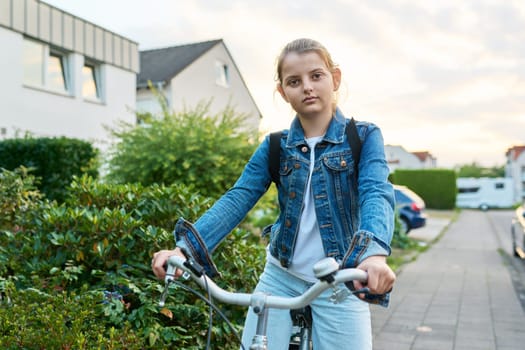 Back to school. Girl child 10, 11 years old with backpack on bicycle on street near house, posing looking at camera. Schoolgirl cycling to school, lifestyle, childhood concept