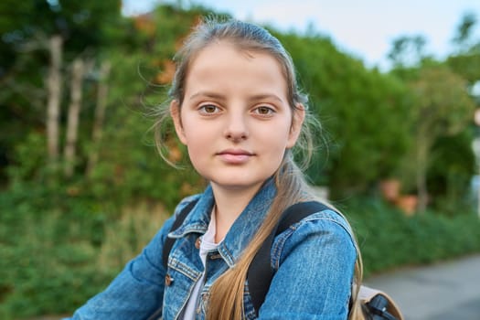 Closeup headshot portrait 10 years old girl posing schoolgirl with backpack outdoor looking at camera. Age 10, 11 children, preteens, school, lifestyle, childhood concept