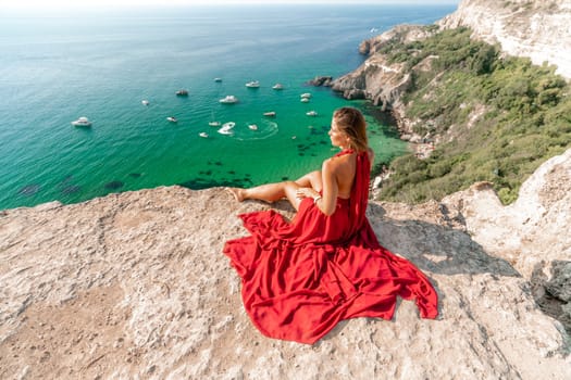 Woman sea red dress yachts. A beautiful woman in a red dress poses on a cliff overlooking the sea on a sunny day. Boats and yachts dot the background