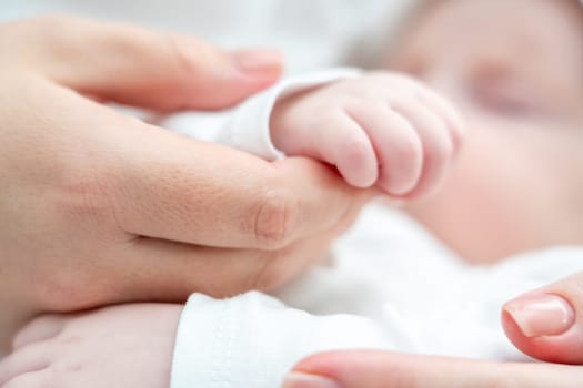 Close-up portrays a sleeping newborn baby softly gripping mother's finger, symbolizing trust and care