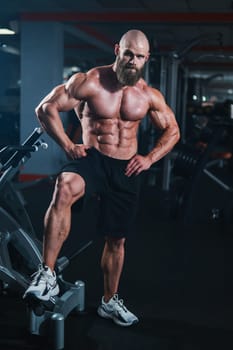 Muscular bald man posing in shorts. Bodybuilder showing off his shape in the gym