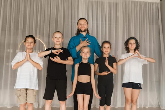 A joint portrait of a yoga coach and children standing in a fitness room.