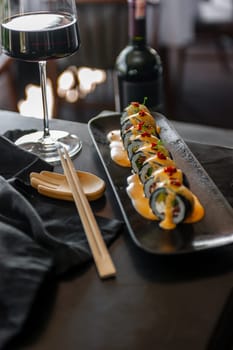 Sushi roll with tuna and vegetables in sauce on a black plate in a restaurant. High quality photo