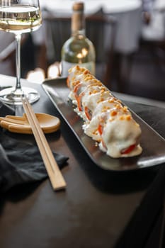 Sushi roll with salmon and vegetables in sauce on a black plate in a restaurant. High quality photo