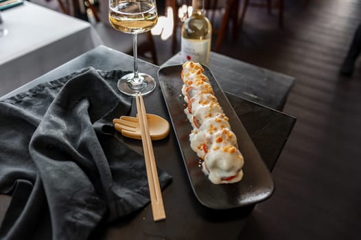 Sushi roll with salmon and vegetables in sauce on a black plate in a restaurant. High quality photo