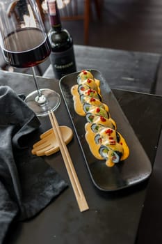 Sushi roll with tuna and vegetables in sauce on a black plate in a restaurant. High quality photo
