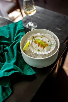 Scallop in sauce with flying fish caviar on a shell on ice in a restaurant. High quality photo