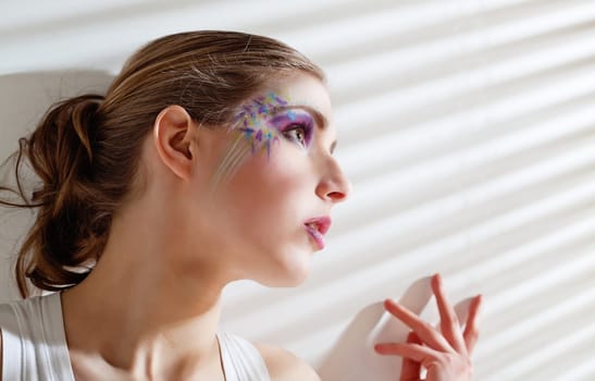 Pretty young woman lean lit by bright sunlight coming through the blinds
