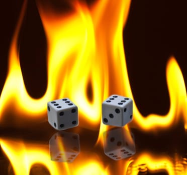 A pair of dice with double sixes lying amidst burning flames with reflection