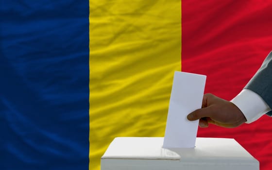 man putting ballot in a box during elections  in front of national flag of chad