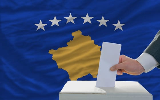 man putting ballot in a box during elections  in front of national flag of kosovo