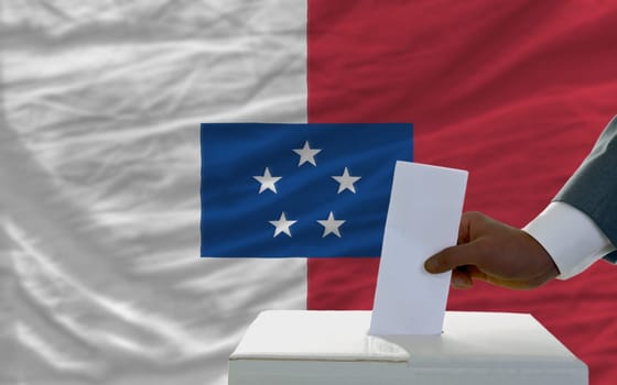 man putting ballot in a box during elections  in front of national flag of franceville