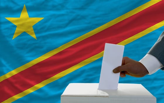 man putting ballot in a box during elections  in front of national flag of congo