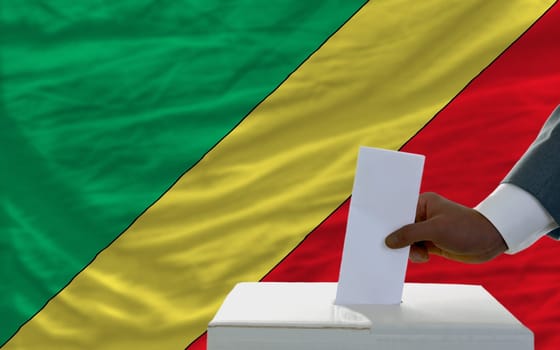 man putting ballot in a box during elections  in front of national flag of congo