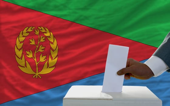 man putting ballot in a box during elections  in front of national flag of eritrea